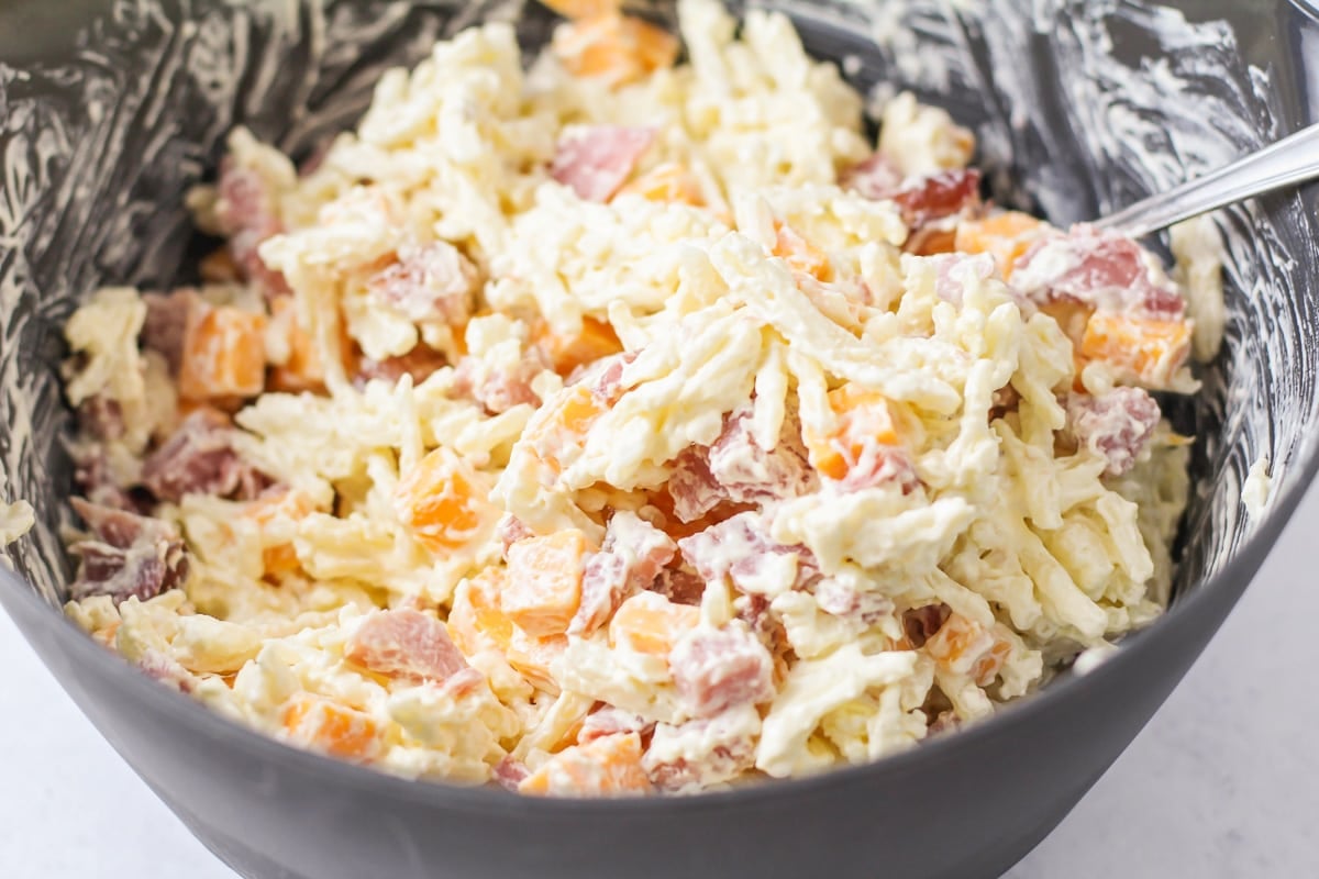 Mixing hashbrowns, cheese, and ham in a bowl.