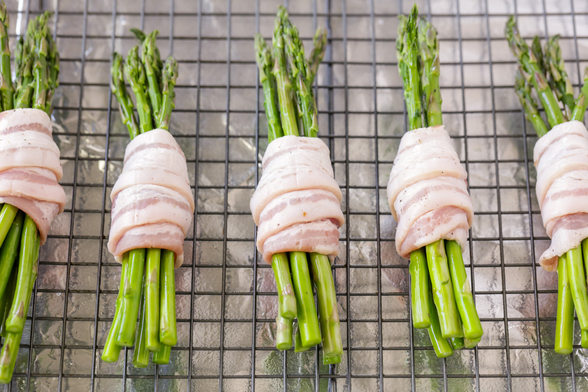 Seasoned bacon wrapped asparagus bundles on a baking sheet ready to bake.