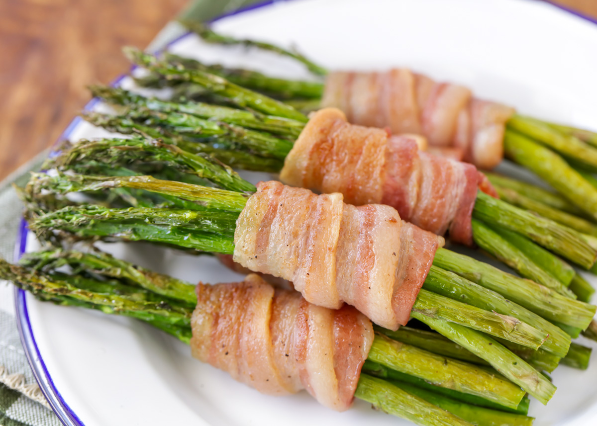 Bacon wrapped asparagus bundles on a white plate.