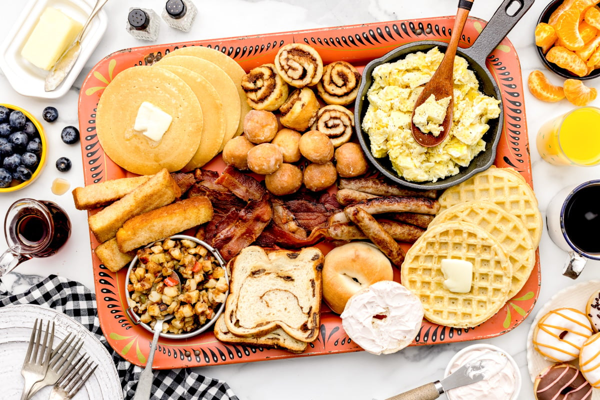 A breakfast charcuterie board with various breakfast foods on an orange platter. 