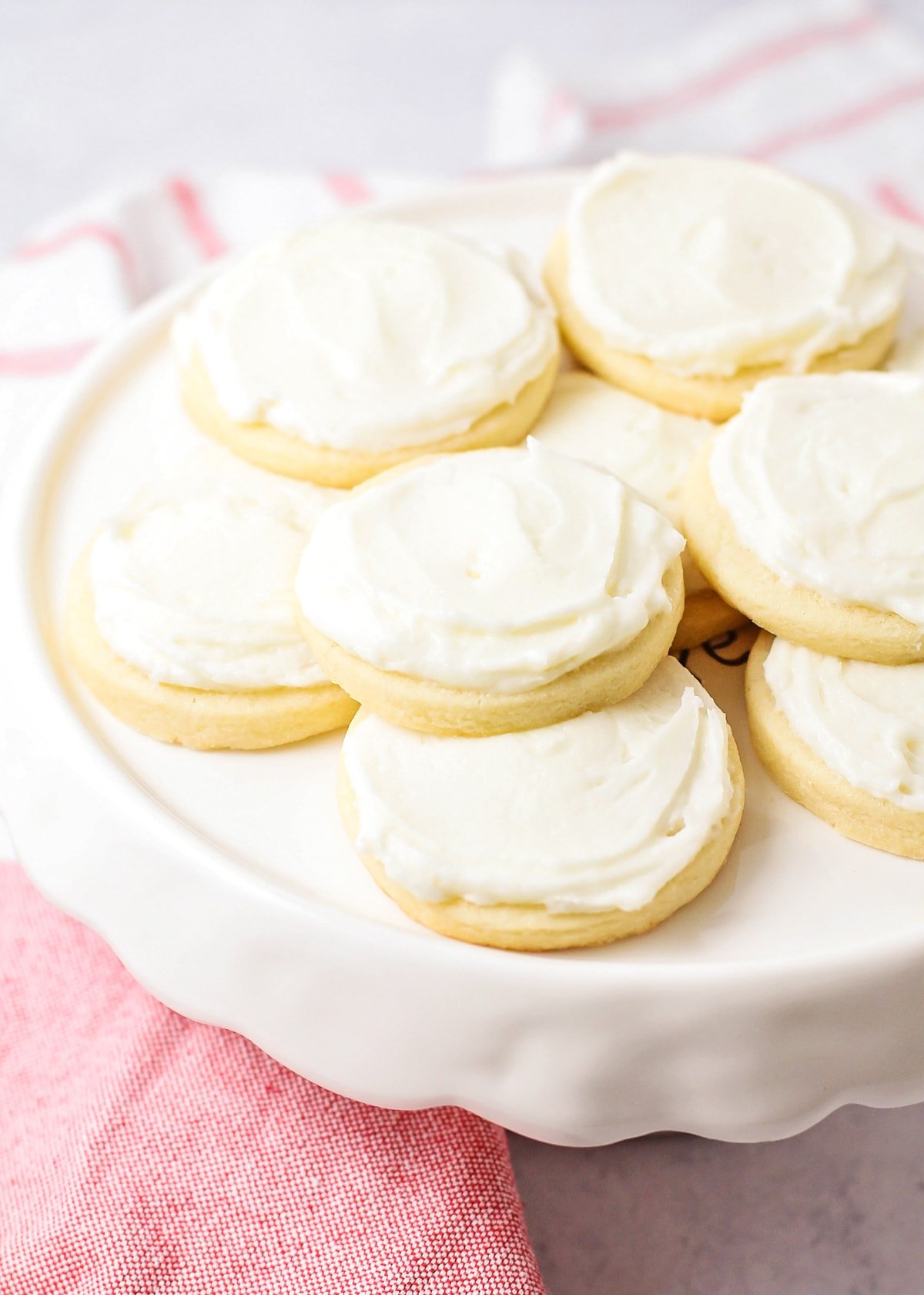 Frosted butter cookies stacked on a white cake platter.