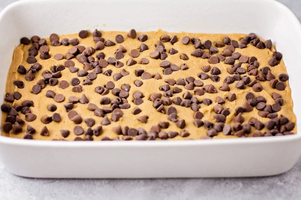 Chocolate chips sprinkled over cookie dough in a white baking dish.