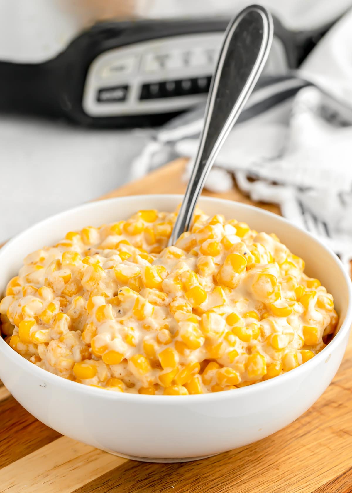 A spoon stuck in a white bowl filled with slow cooker creamed corn.