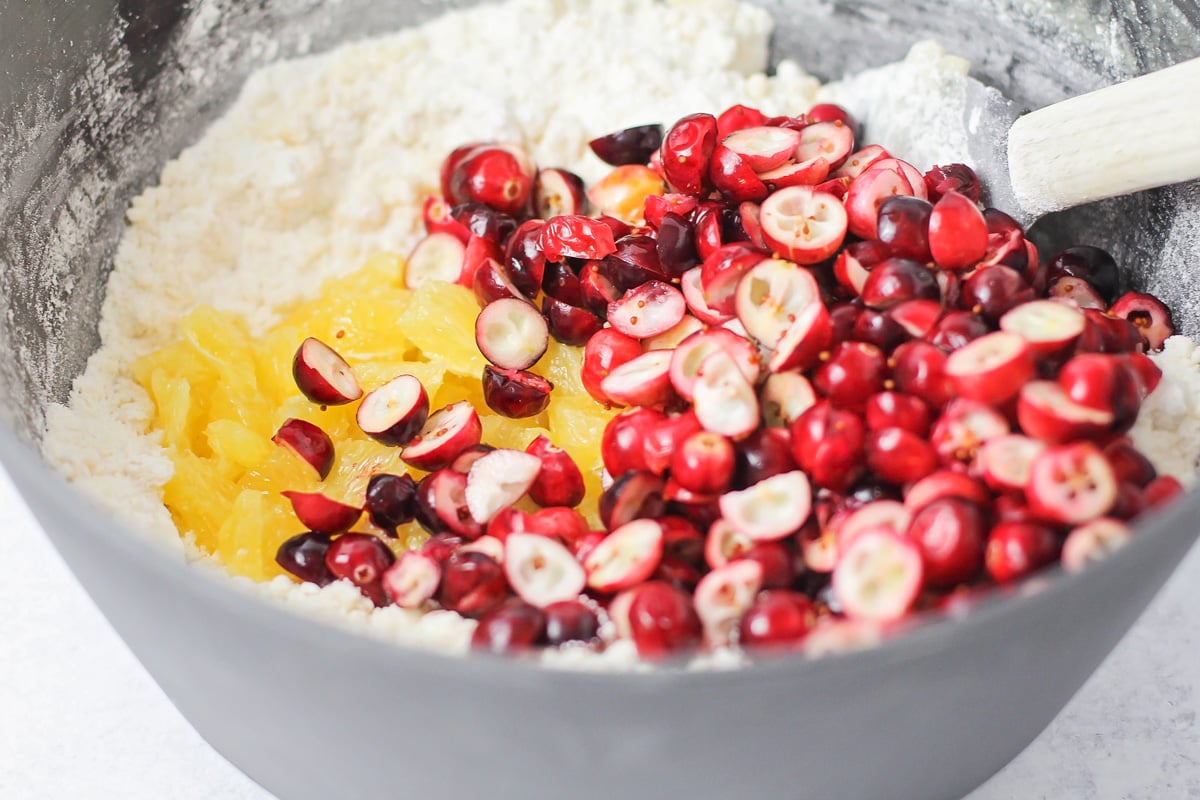 Adding sliced cranberries and oranges to a bowl of dry ingredients.