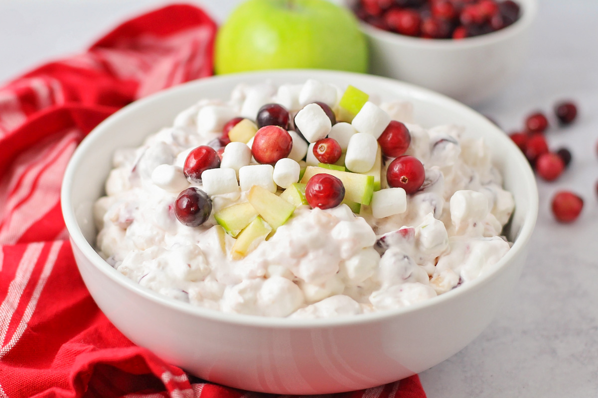 Close up of a bowl filled with cranberry salad topped with fresh apples and cranberries.