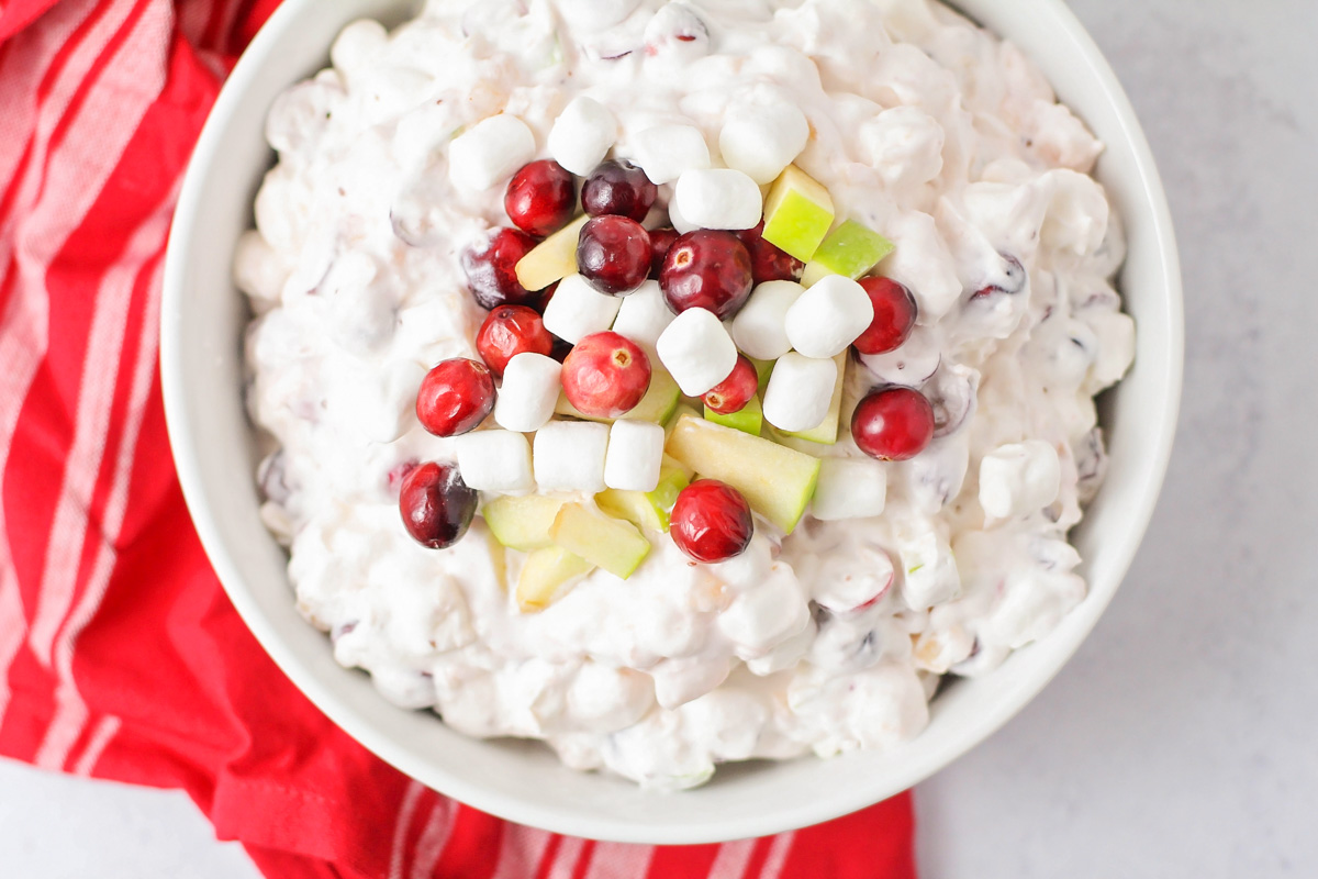 Close up of a bowl of cranberry salad garnished with apples, cranberries, and marshmallows.