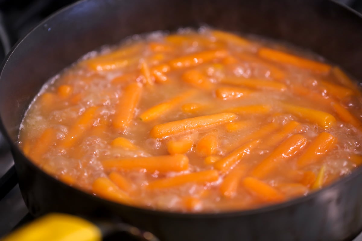 Baby carrots boiling in water, butter and brown sugar to become glazed carrots.