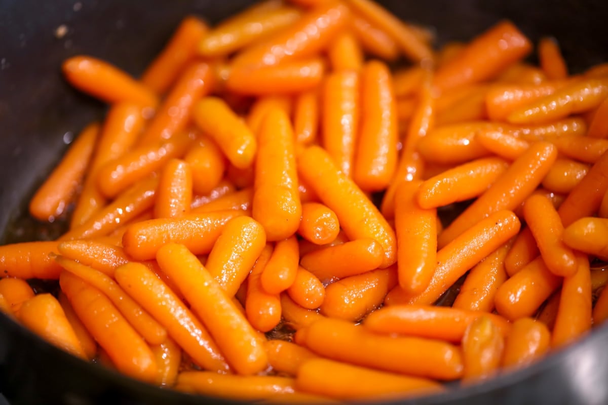 Glazing baby carrots in a black pot.