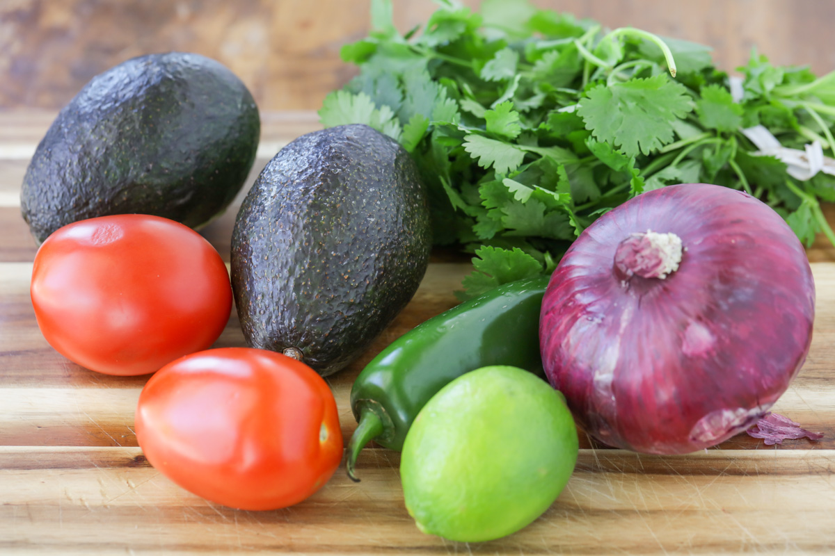 Ingredients for guacamole recipe on a wood cutting board.