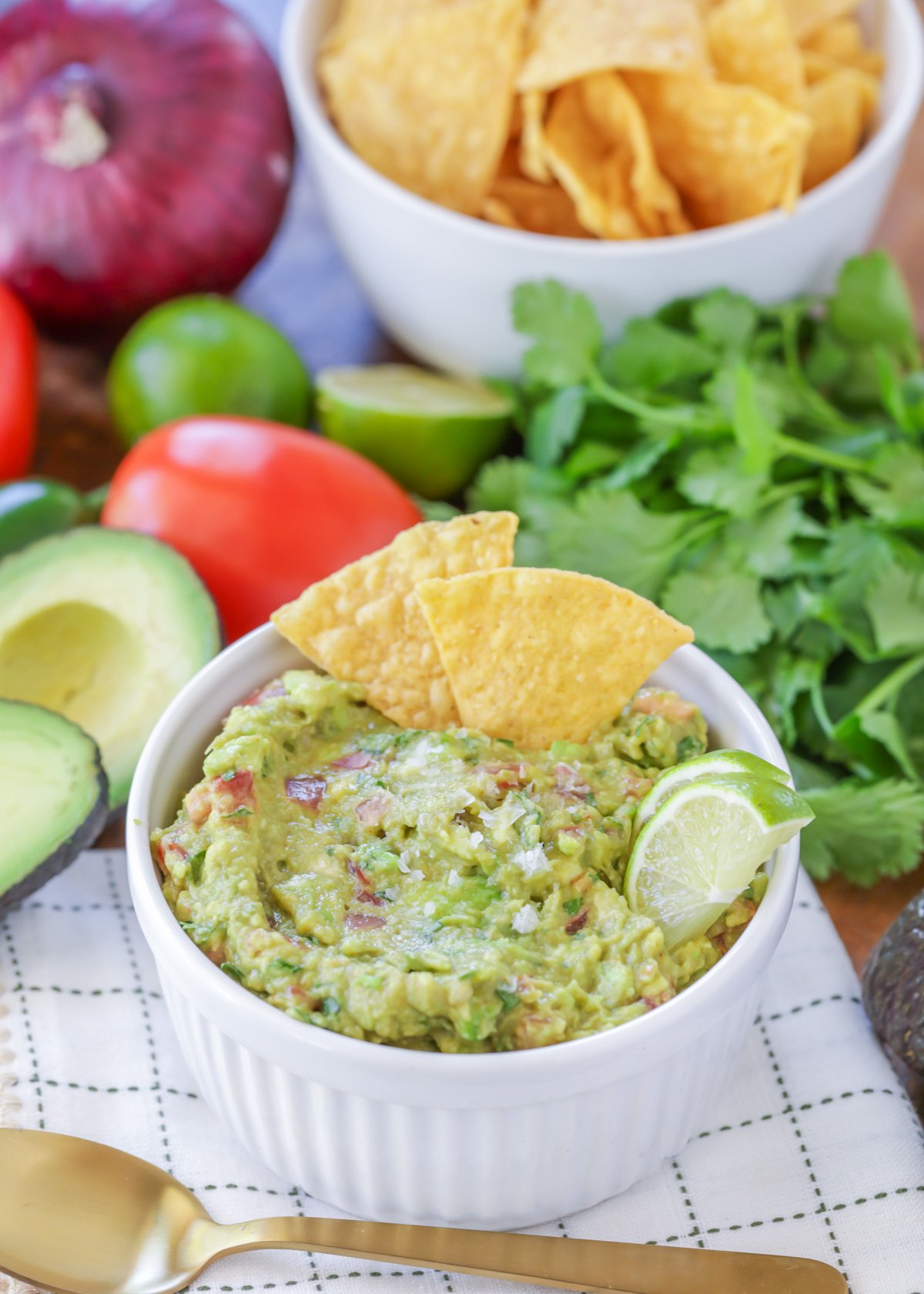 Easy guacamole in a small white bowl with tortilla chips, lime slices, and sea salt on top.