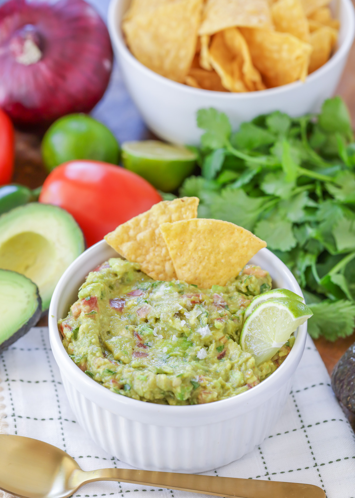 Easy guacamole recipe in a small white bowl with tortilla chips, lime slices, and sea salt on top.