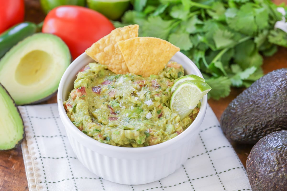 Guacamole in a white ramekin garnished with two corn tortilla chips and two lime wedges. 