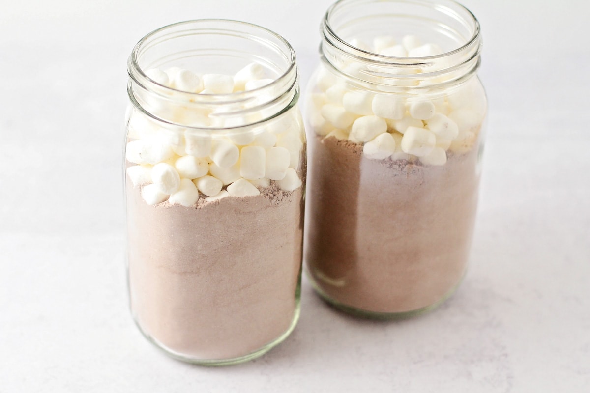 Filling mason jars with mix and marshmallows for a hot chocolate gift.