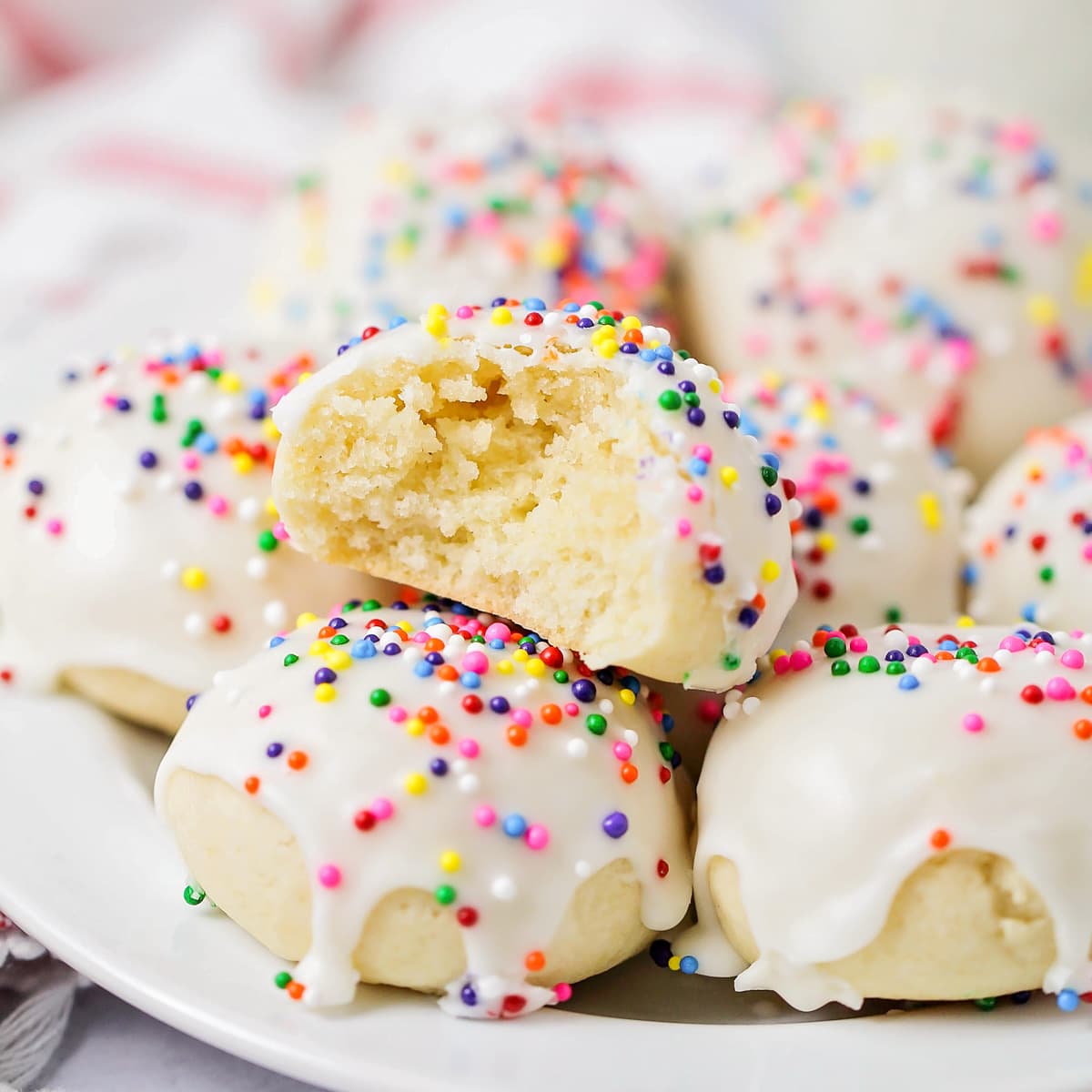 Italian Cookies topped with glaze and sprinkles with one missing a bite.