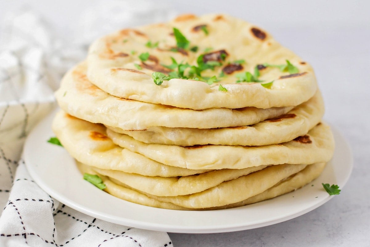 Easy naan bread stacked on top of each other on white plate.