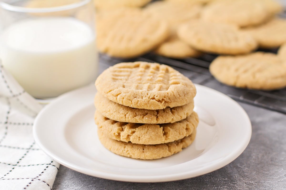 A stack of peanut butter cookies on a white plate served with milk.