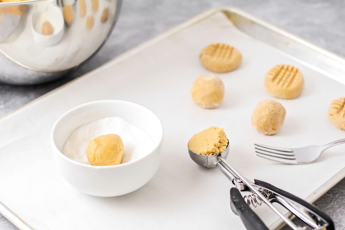Scooping and coating peanut butter cookie dough balls in sugar.