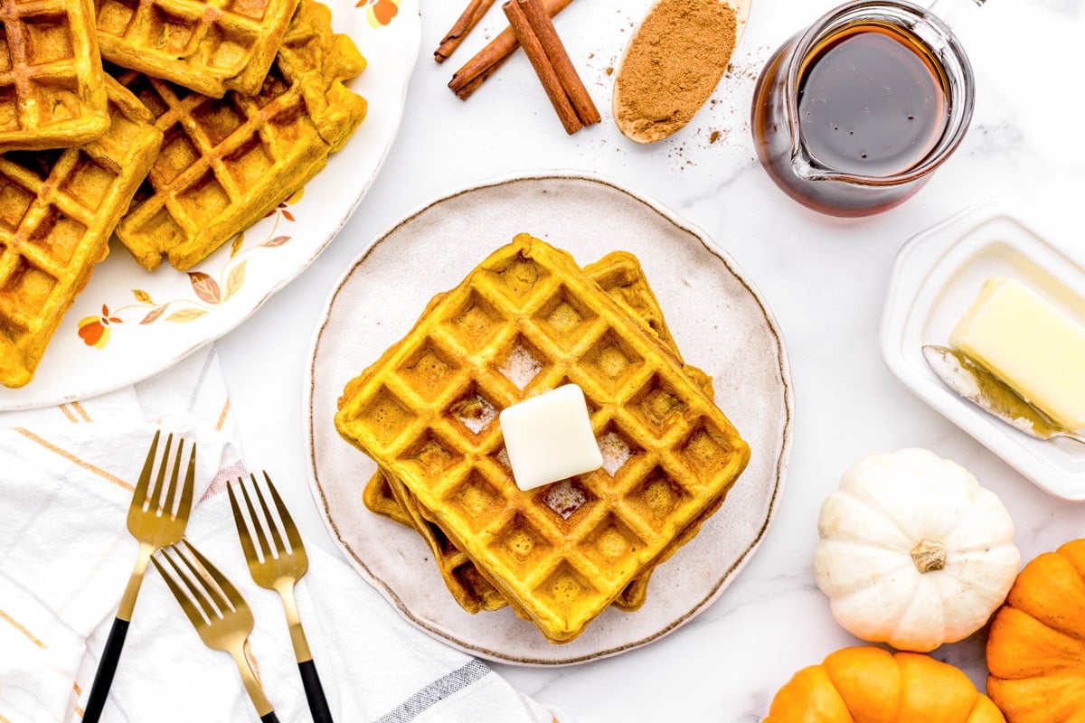 Stack of pumpkin waffles topped with butter and syrup.