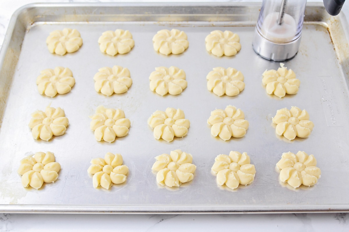 Placing shortbread cookies recipe on a baking sheet with a cookie press.