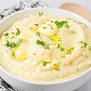 A bowl of crock pot mashed potatoes topped with butter and herbs.