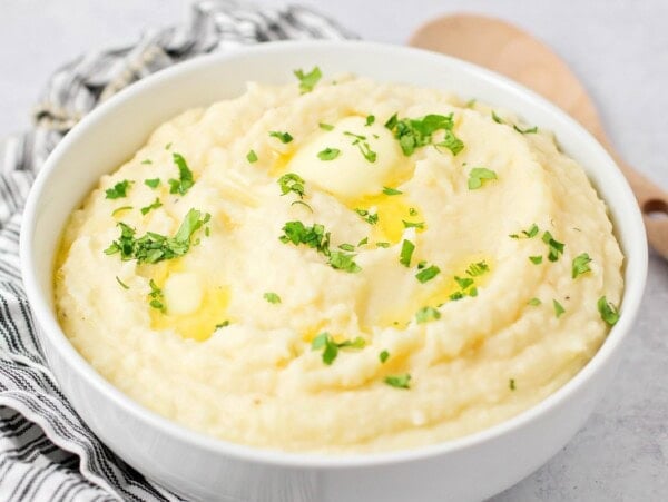 A bowl of crock pot mashed potatoes topped with butter and herbs.