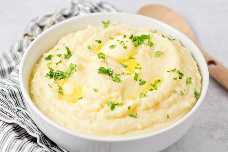 A bowl of crock pot mashed potatoes topped with butter and herbs.