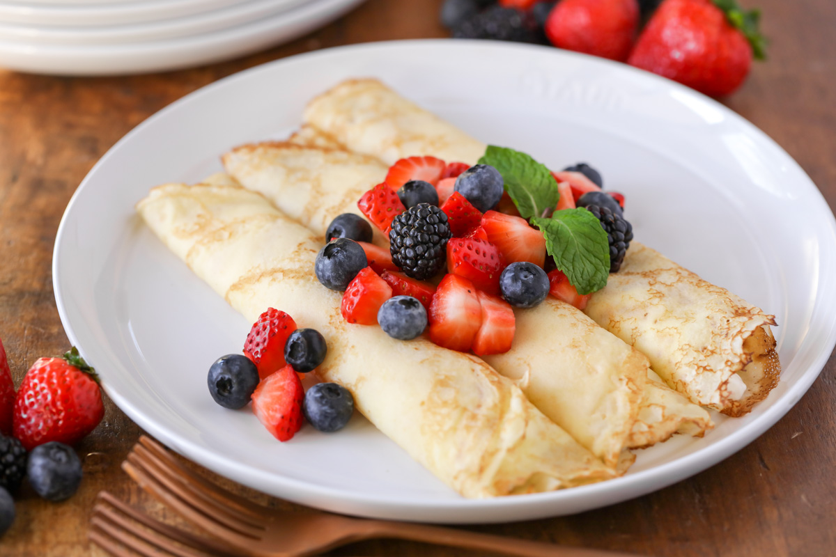 Three swedish pancakes topped with berries and mint.