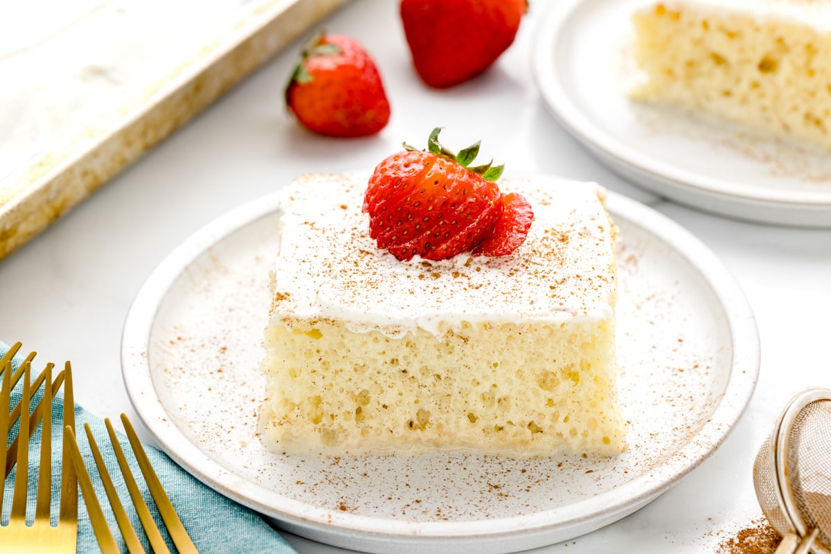 Tres leches cake on a plate, topped with a strawberry and cinnamon.