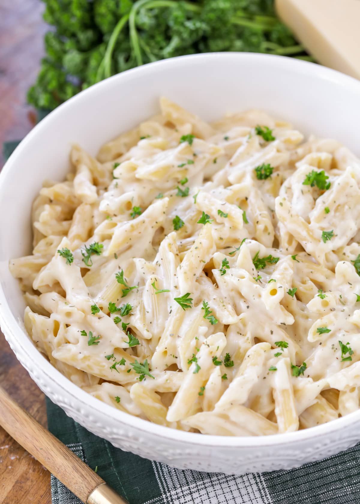 White Sauce recipe covered on penne pasta sprinkled with parsley in white bowl.