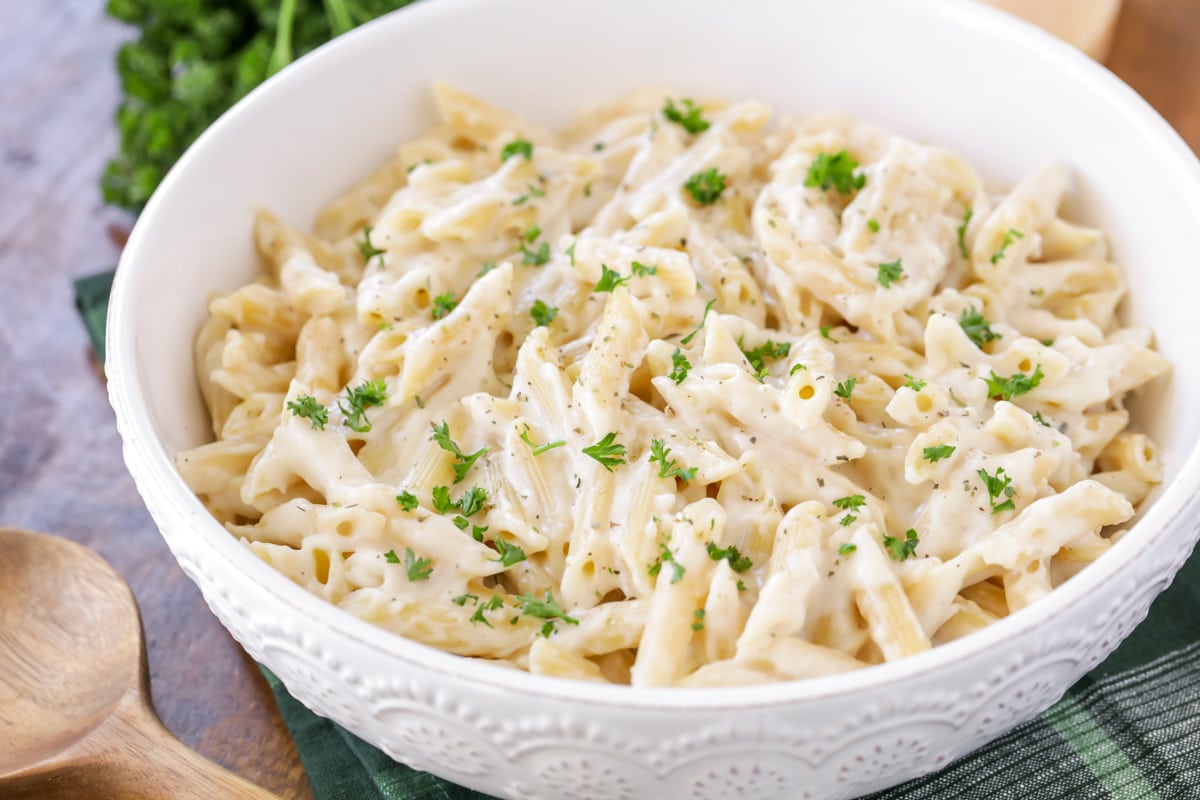 White sauce recipe on top of penne pasta topped with fresh herbs.