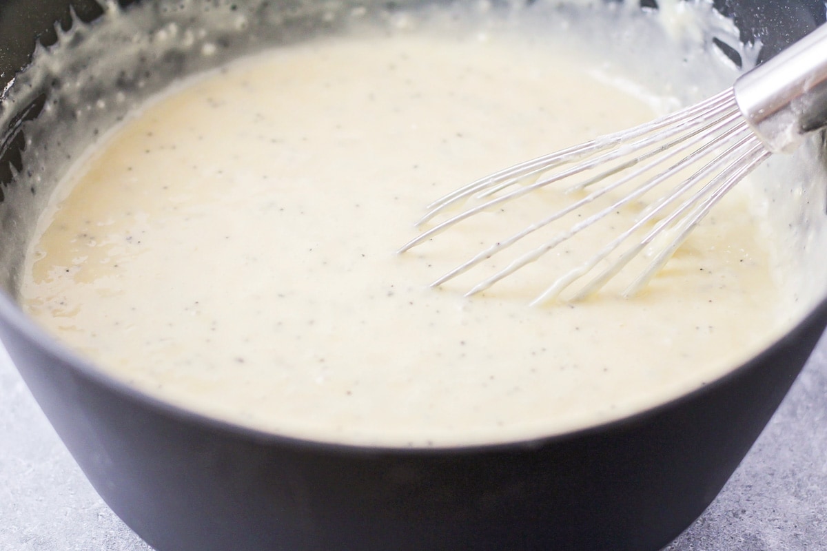 Mixing ingredients for almond poppy seed bread recipe with a whisk.