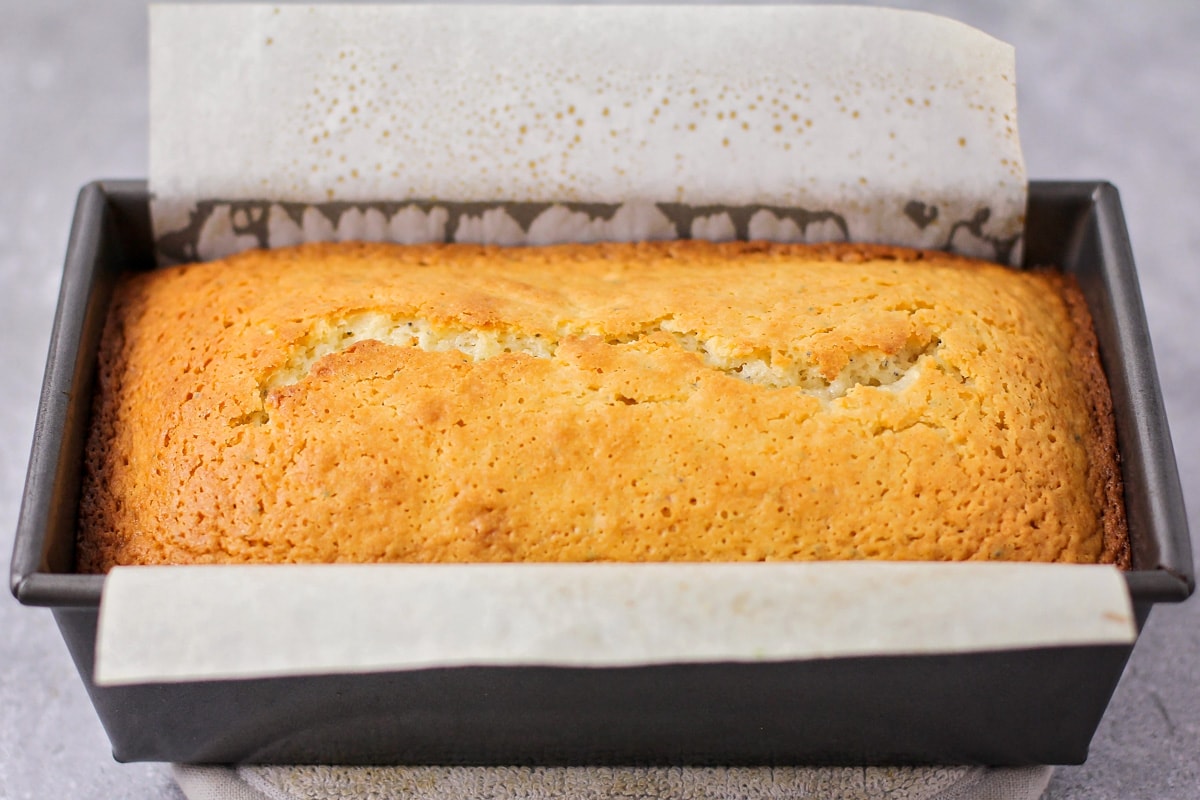 Baked almond poppyseed bread in a loaf pan lined with parchment paper.