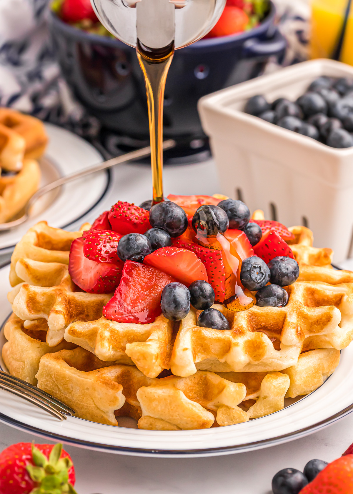 Pouring syrup on a Bisquick waffle recipe topped with berries.