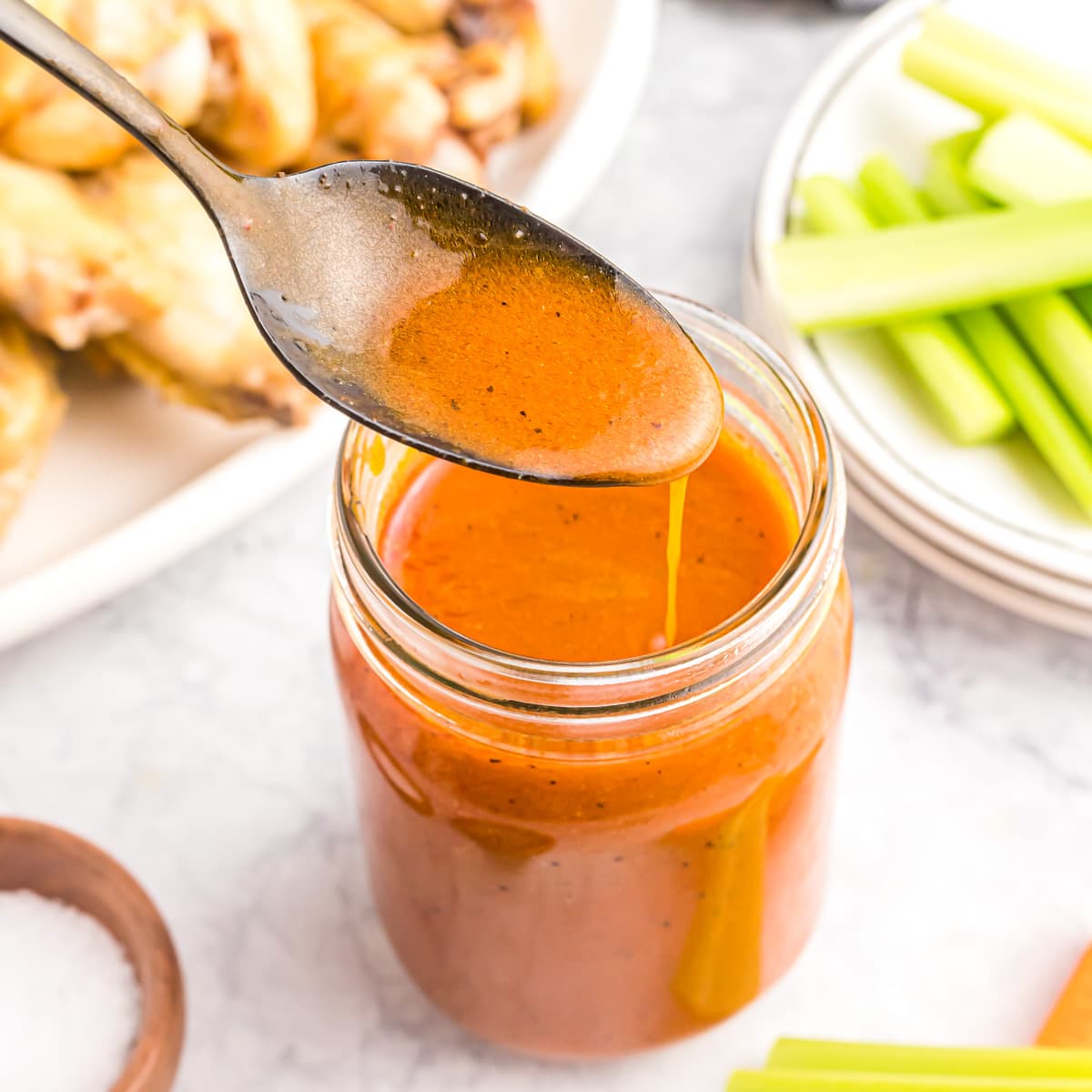 A spoon dripping buffalo sauce recipe into a mason jar.