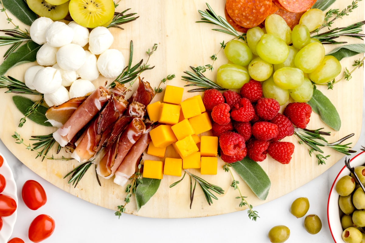 A wreath charcuterie board with cubed cheese, fresh fruit and herbs.