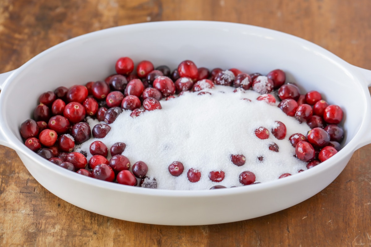 Combining cranberries and sugar in a white serving dish.