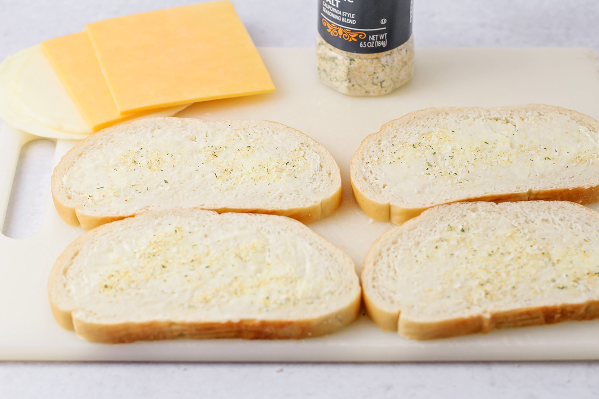 Spreading butter and garlic salt on bread slices to make homemade grilled cheese.
