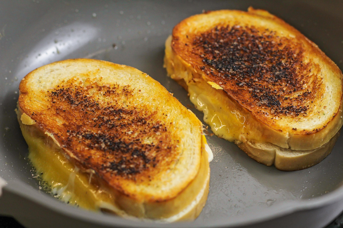 Two grilled cheese sandwiches cooking in a pan.