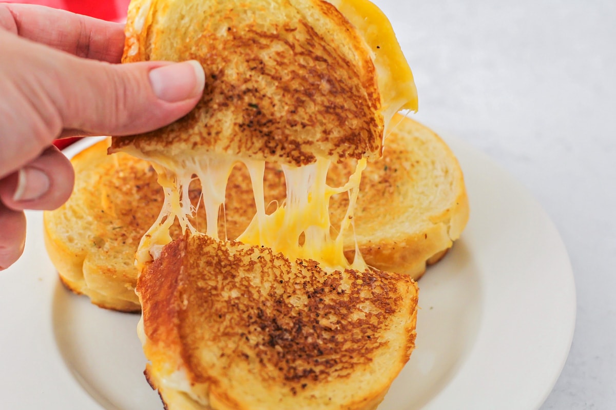 A hand pulling apart a grilled cheese sandwich.