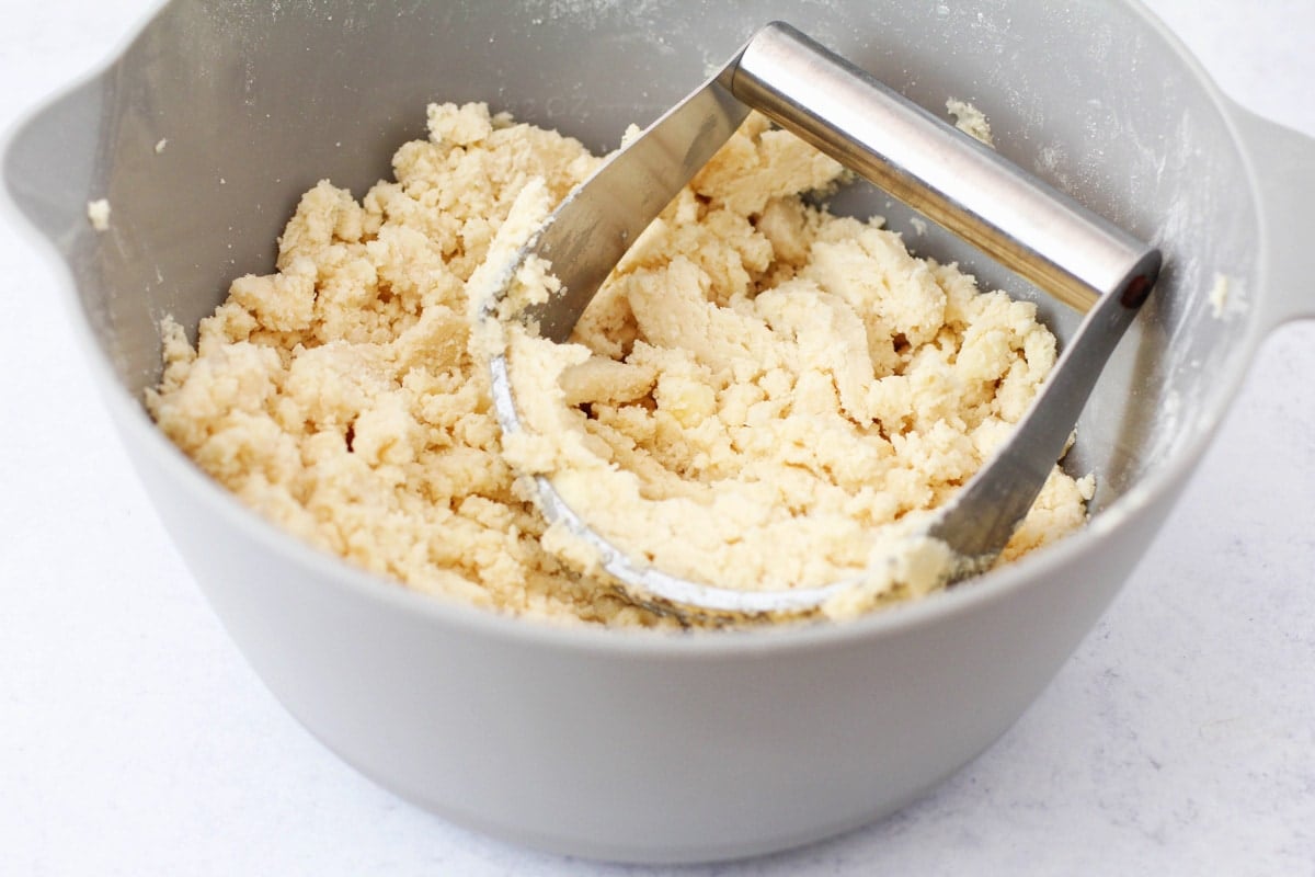 A pastry cutter in a mixing bowl with the dough for lemon bar crust.