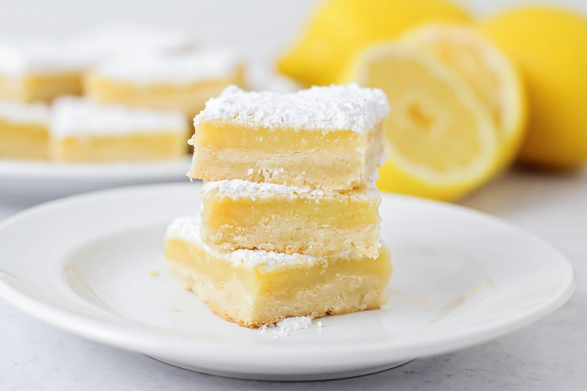 A stack of three lemon bars on a white plate.