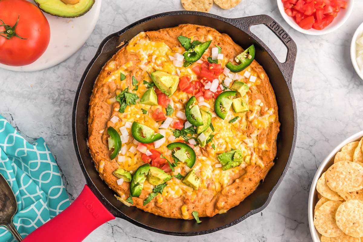 Hot Mexican bean dip bake in a skillet and topped with fresh jalapeno and avocado.