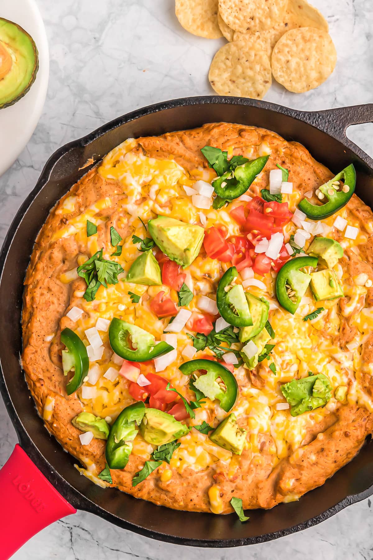 Close up of Mexican bean dip baked in a skillet topped with jalapeno and avocado.