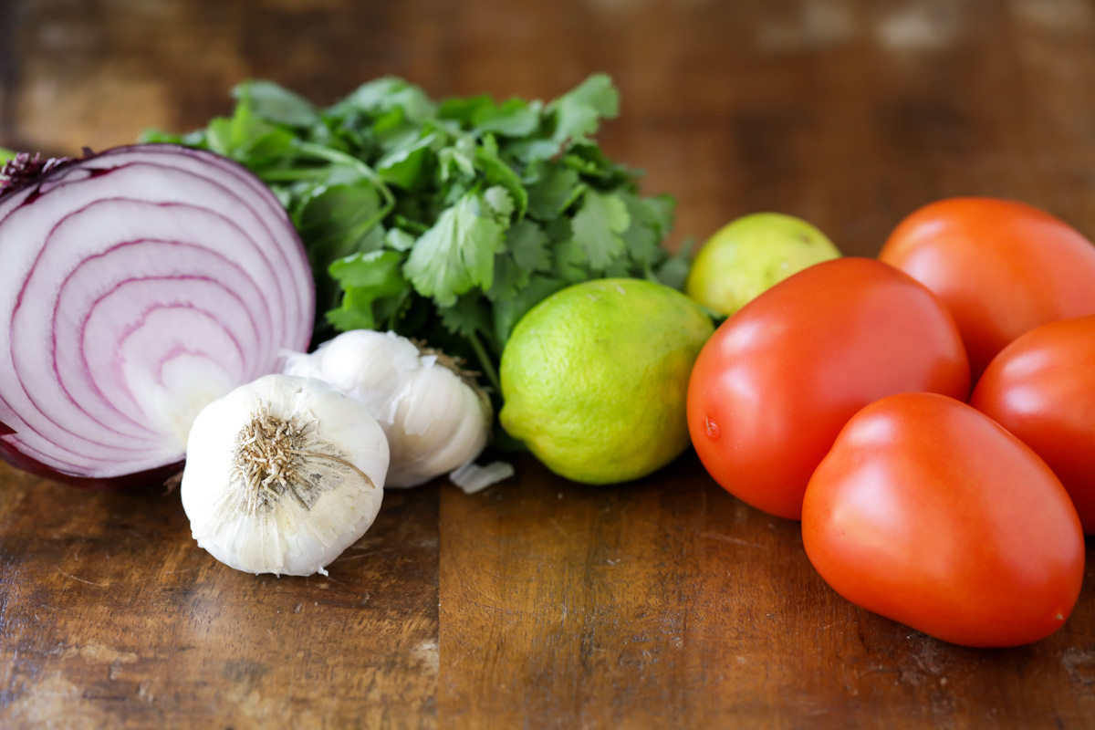 Tomatoes, onion, garlic, and cilantro on a wooden counter.