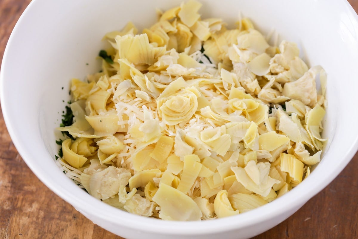 Mixing spinach and artichoke in a white bowl.