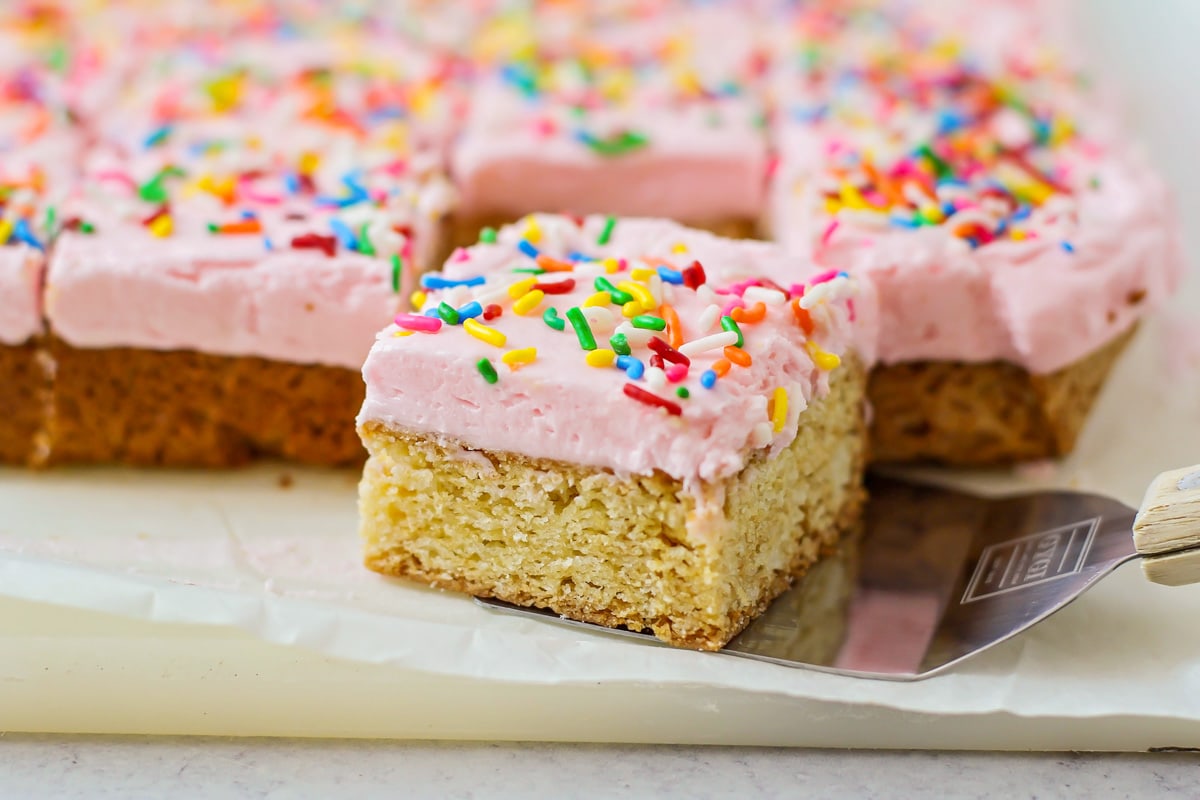 Sugar cookie bars with spatula near it on parchment paper.