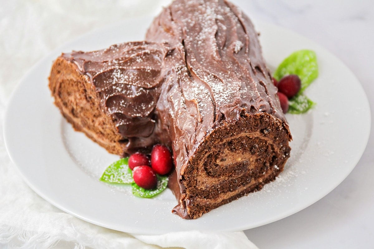 Yule Log Cake decorated and served on a white plate.
