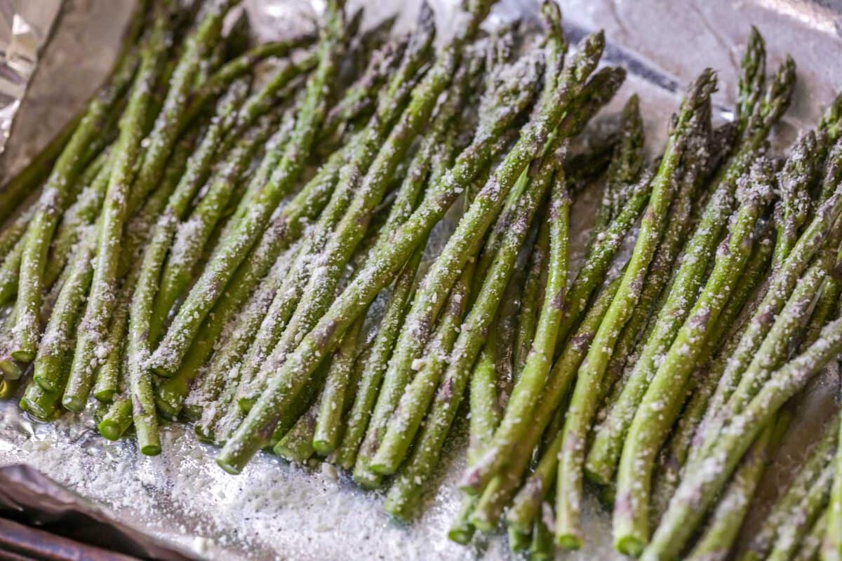 Asparagus covered in parmesan cheese an seasonings on a lined baking sheet.