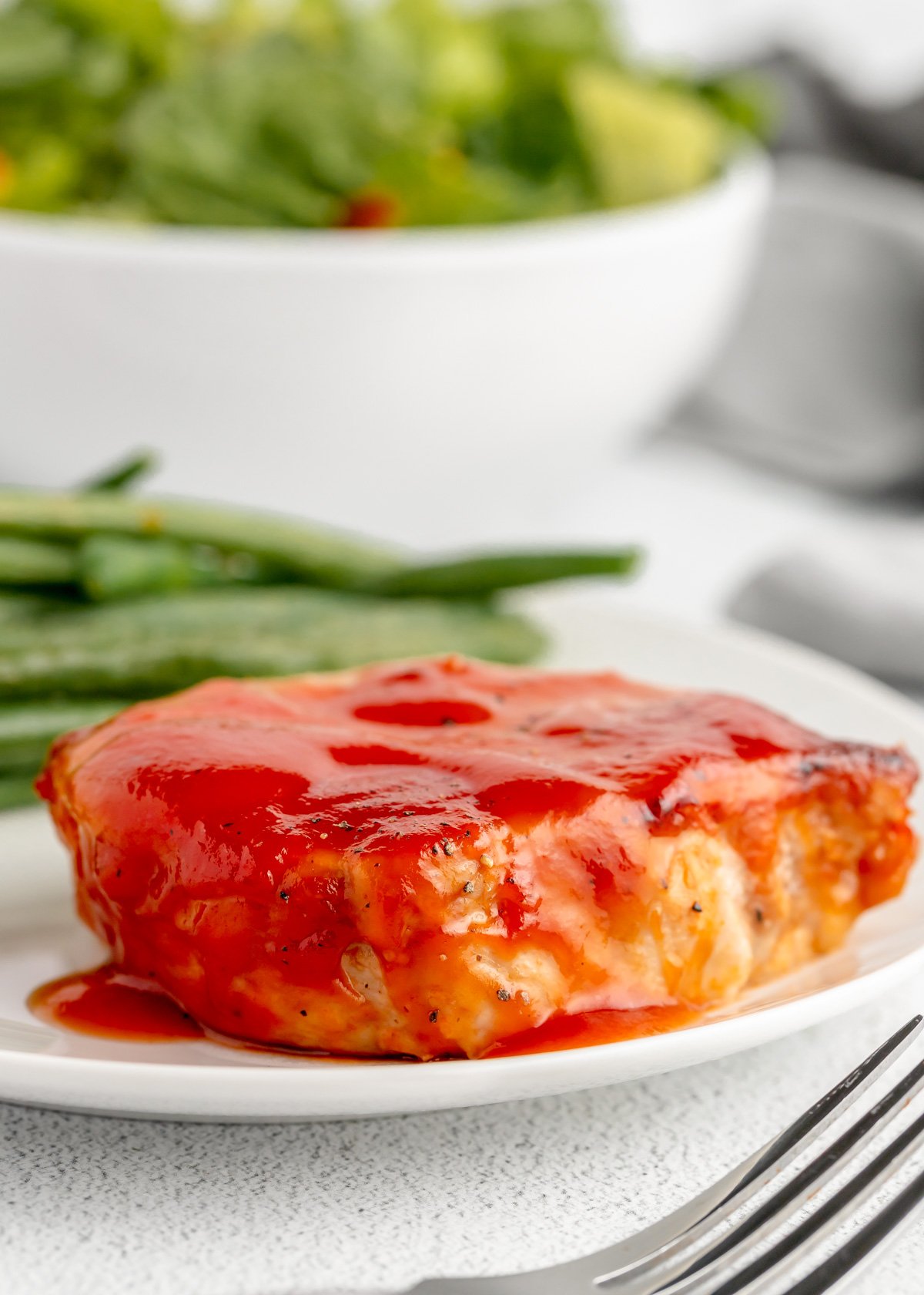 Close up of a smothered baked bbq pork chop served with green beans.