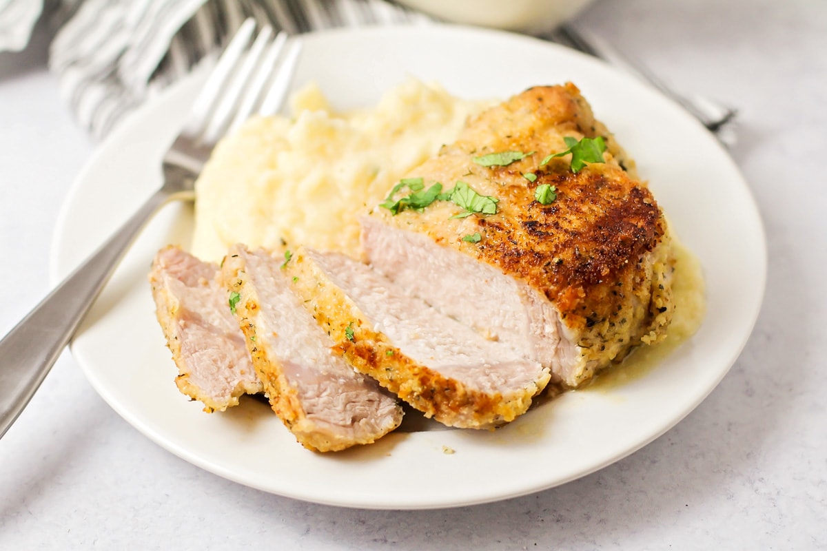 Breaded pork chop on a white plate with mashed potatoes.